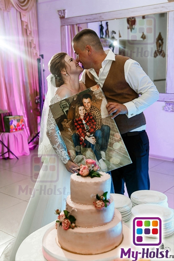 Свадебная пара стоят нос к носу и держат картину со своим изображением